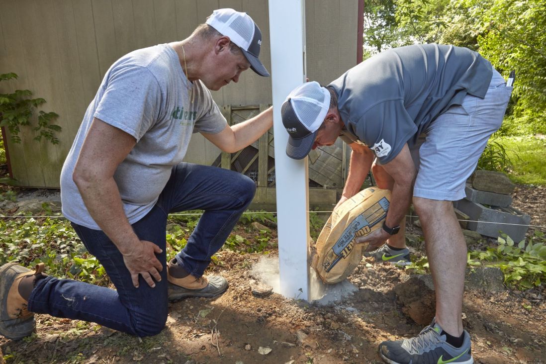 Pros pouring concrete into a hole around a fence post
